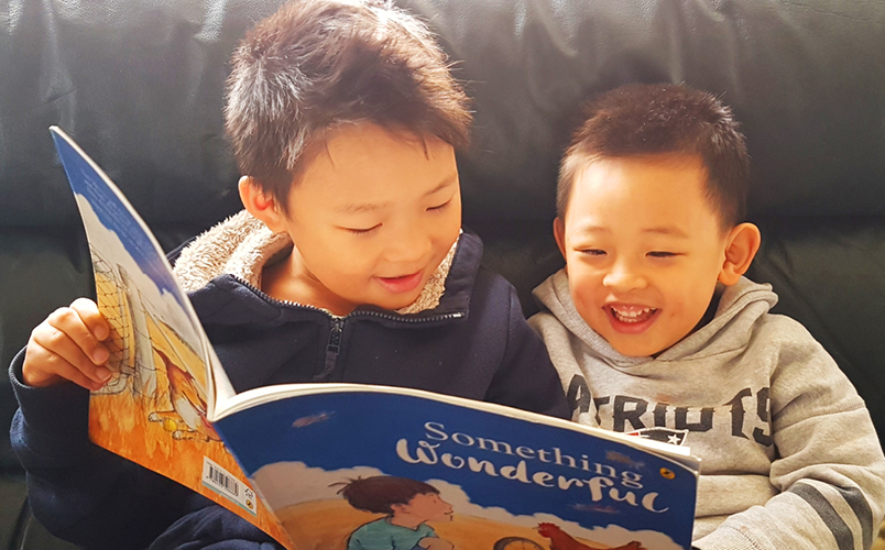 Two boys sit on a couch, reading a book together