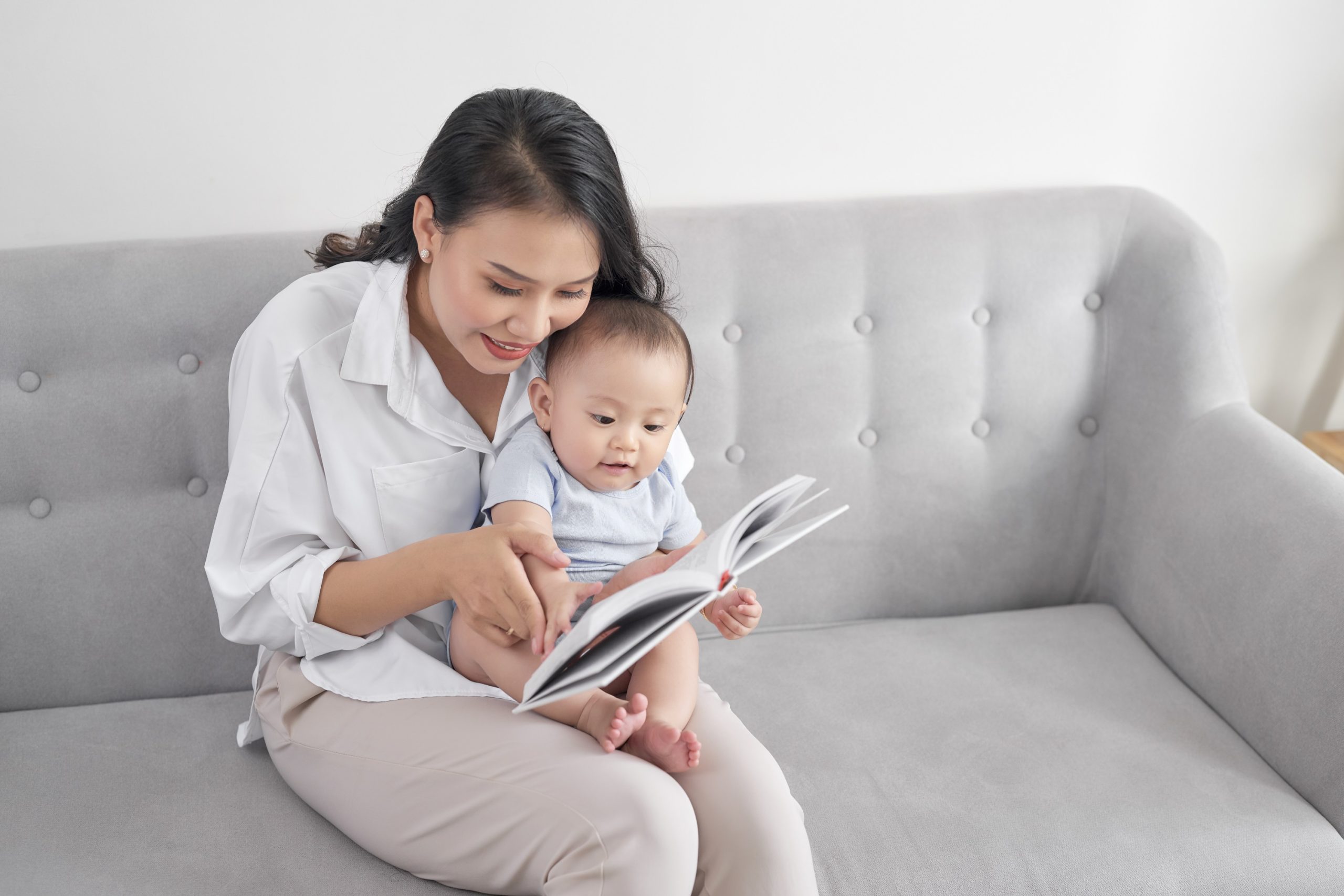 Young asian mother reading book to baby. Sweet moment.